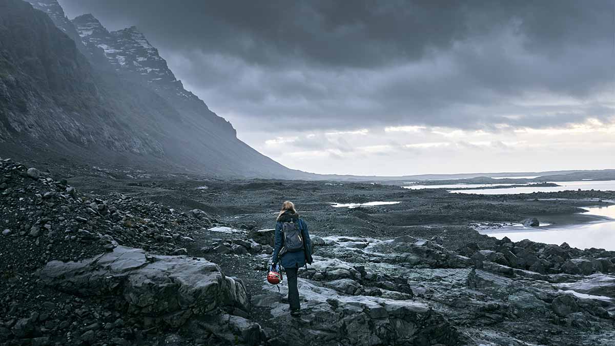 Woman in Iceland holding her motorcycle helmet while walking toward mountains Photo via Pexels, Valdemaras D